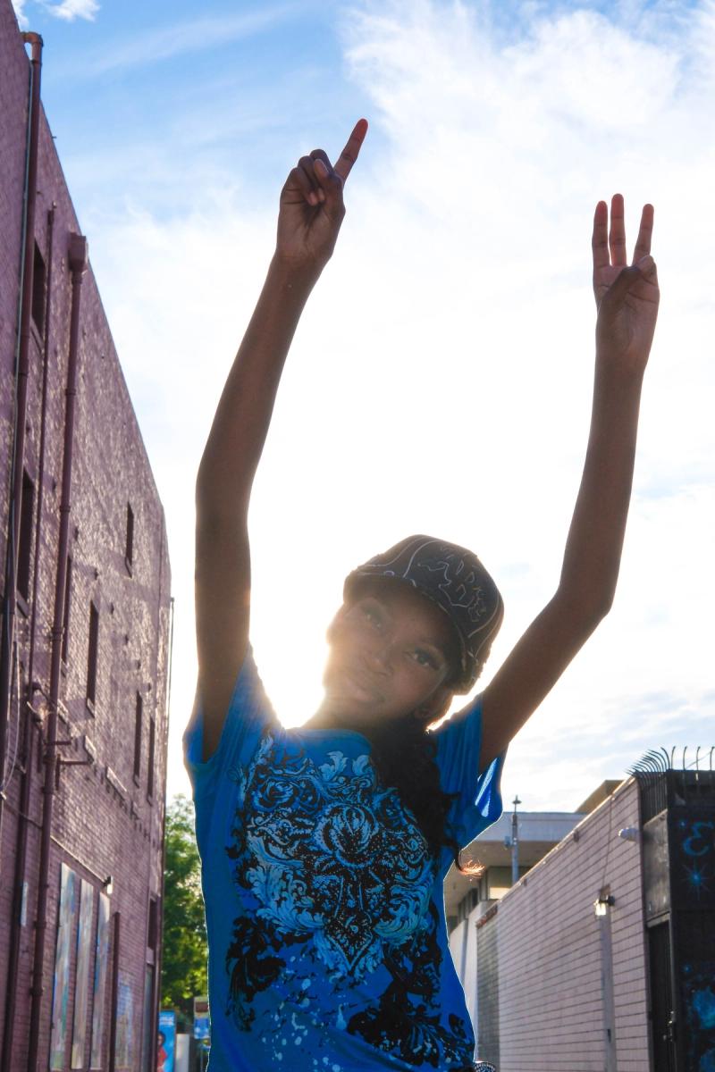 Birthday girl raising peace signs to the sky in a sunlit alley
