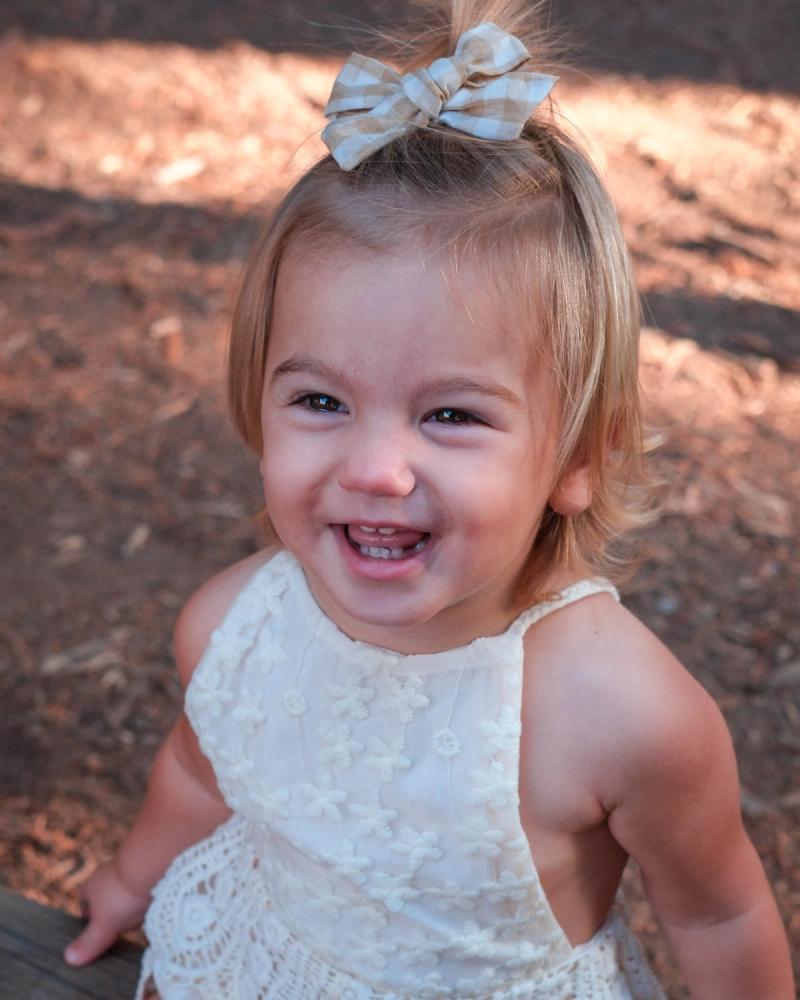 Toddler girl in a lace romper laughing on a log fence