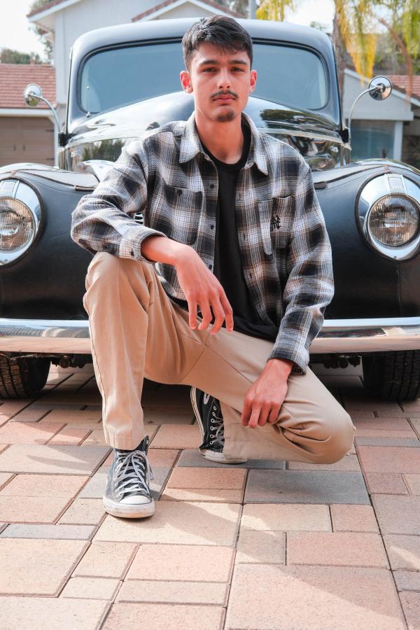 Senior in a plaid flannel crouching in front of a vintage car