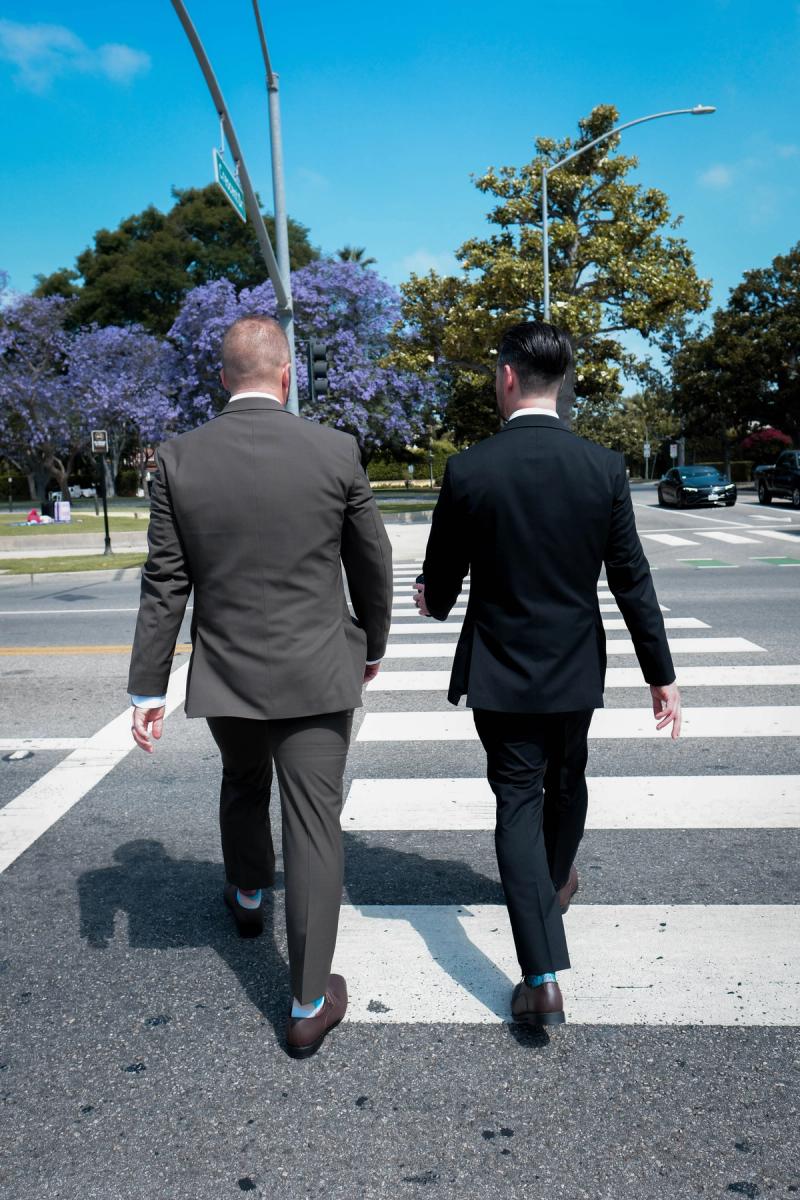 Grooms crossing the street together under purple jacaranda trees