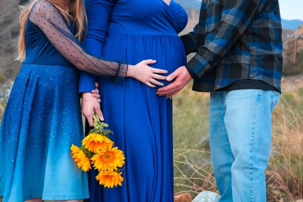 Detail of three hands on the baby bump with sunflowers