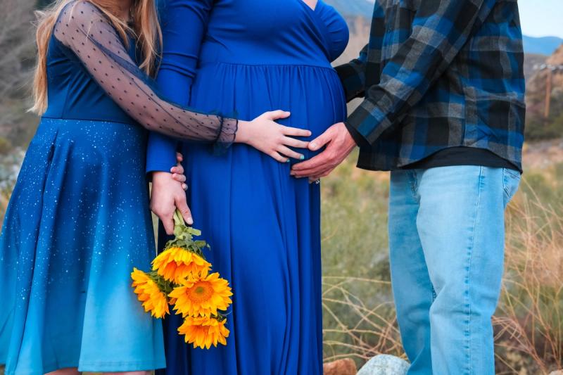Detail of three hands on the baby bump with sunflowers