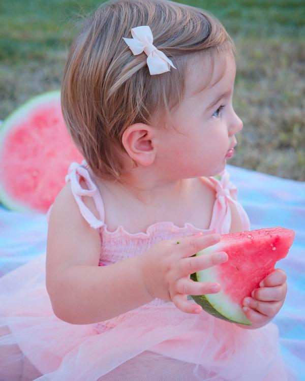 Toddler with a bow in her hair holding a watermelon slice