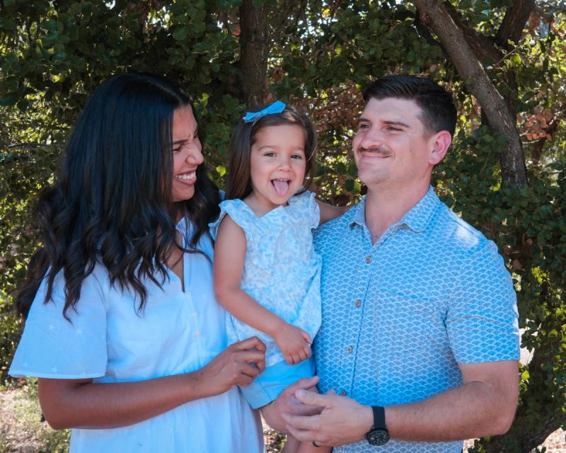 Parents in light blue holding their daughter among the trees