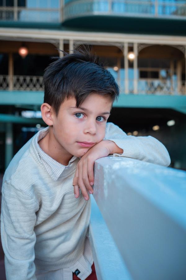 Boy in a cream sweater leaning on a white railing at the racetrack