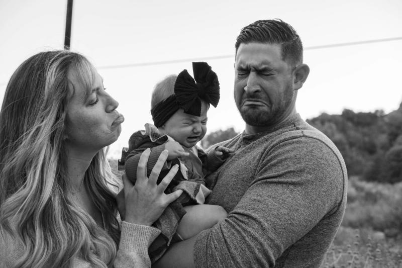 Black and white photo of parents kissing their baby girl in a hair bow