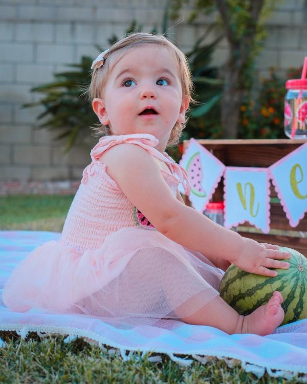 Toddler resting her hand on a whole watermelon and looking up in wonder