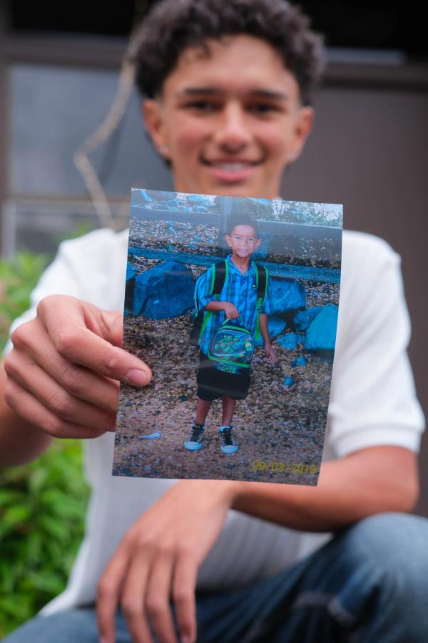 Teen holding up a photo of his younger self at the same school