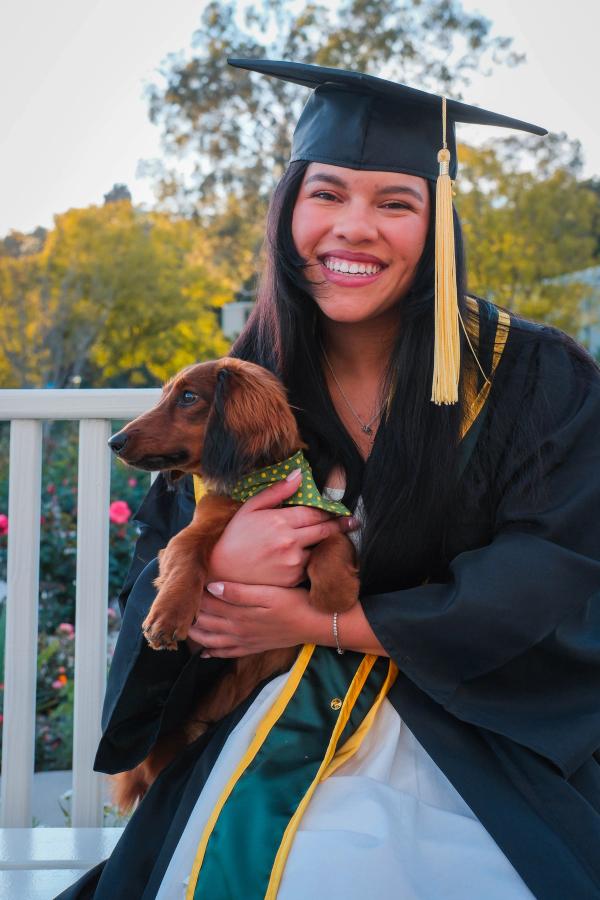 Smiling graduate in cap and gown cuddling her dachshund