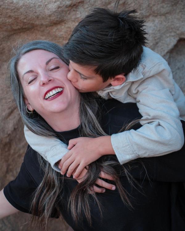 Son hugging his mom from behind and kissing her cheek among desert boulders
