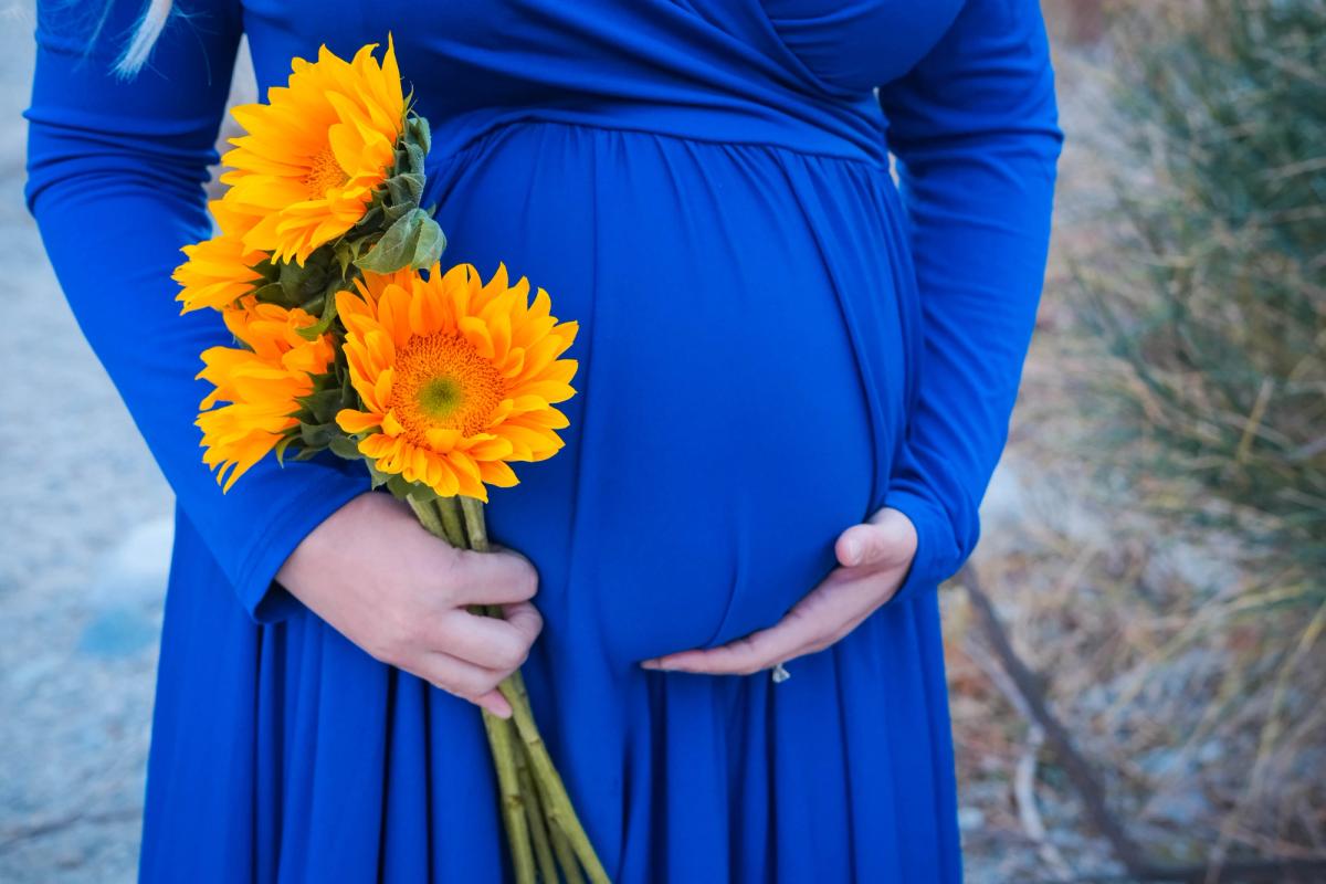 Expecting mother in a royal blue gown holding sunflowers against her bump
