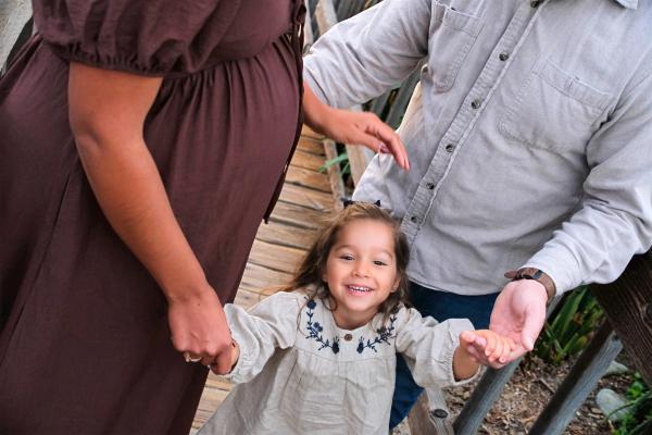 Laughing toddler swinging between her parents on a wooden bridge