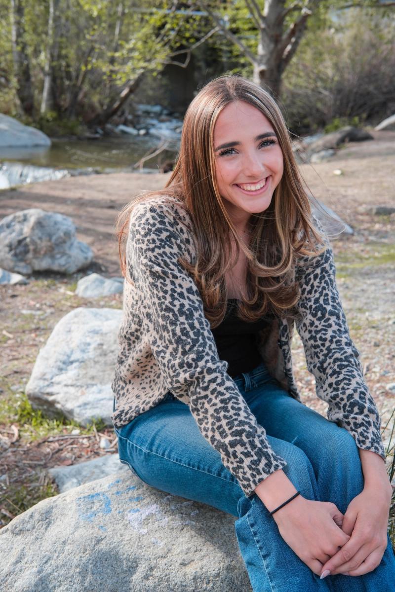 Senior in a leopard print cardigan sitting on a rock by the creek