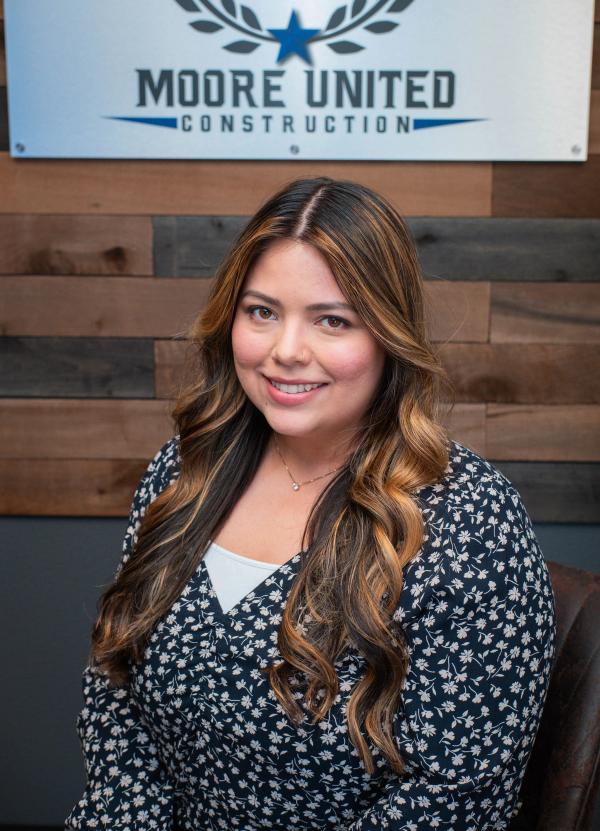 Close headshot of a smiling team member in a floral blouse against reclaimed wood