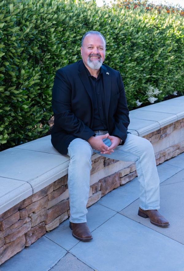 Candidate seated on a stone planter in a black blazer