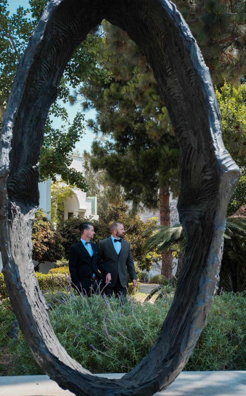 Newlyweds framed through a round bronze sculpture in a garden