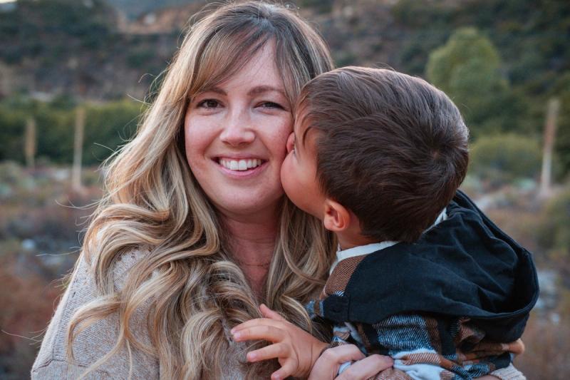 Little boy kissing his mom on the cheek at sunset