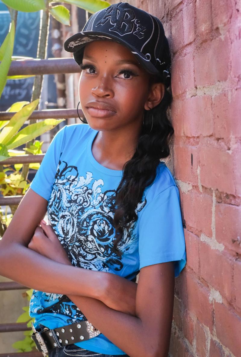 Girl with arms crossed looking up beside a brick wall