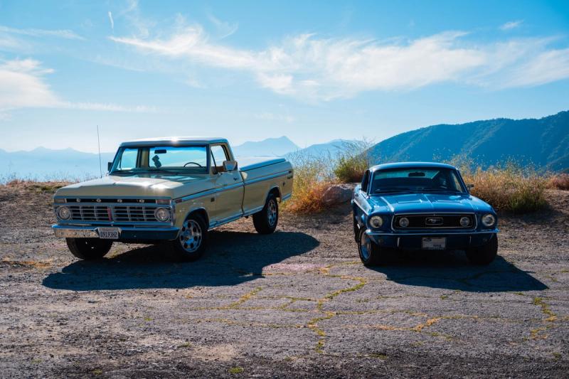 Cream Ford pickup and blue Mustang parked on a mountain overlook