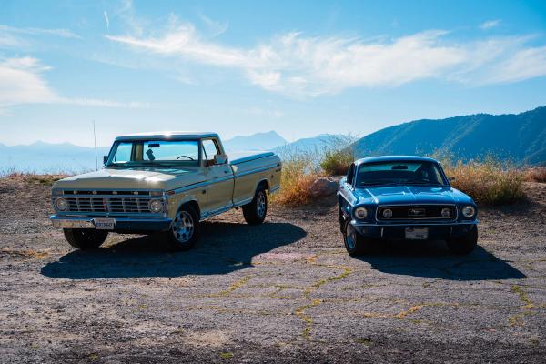 Cream Ford pickup and blue Mustang parked on a mountain overlook