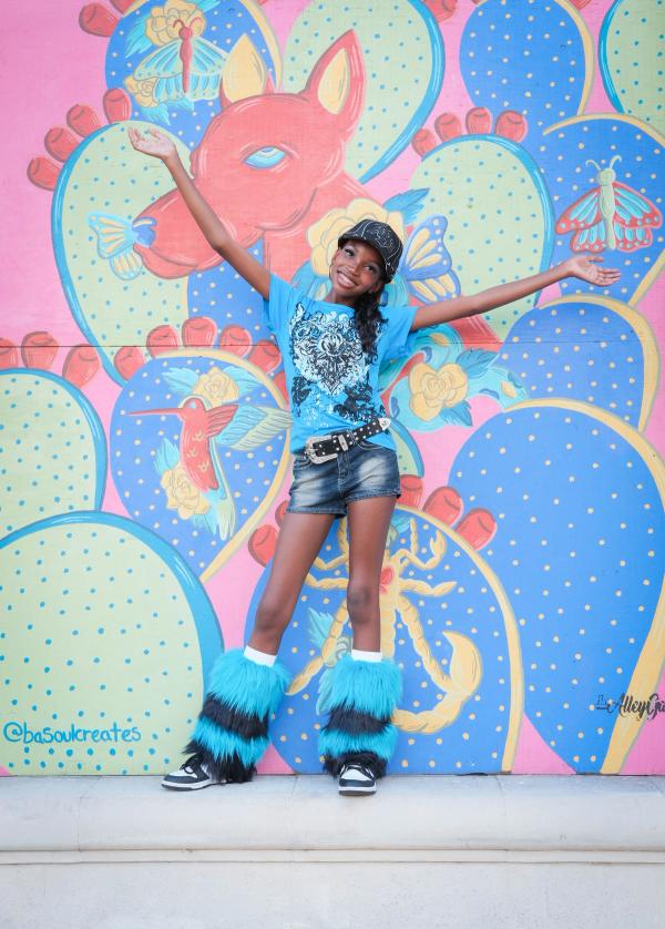 Birthday girl with one arm raised in front of a pink and blue mural