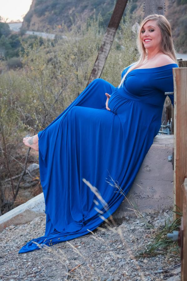Mom-to-be reclining against a wall with her blue gown spread out