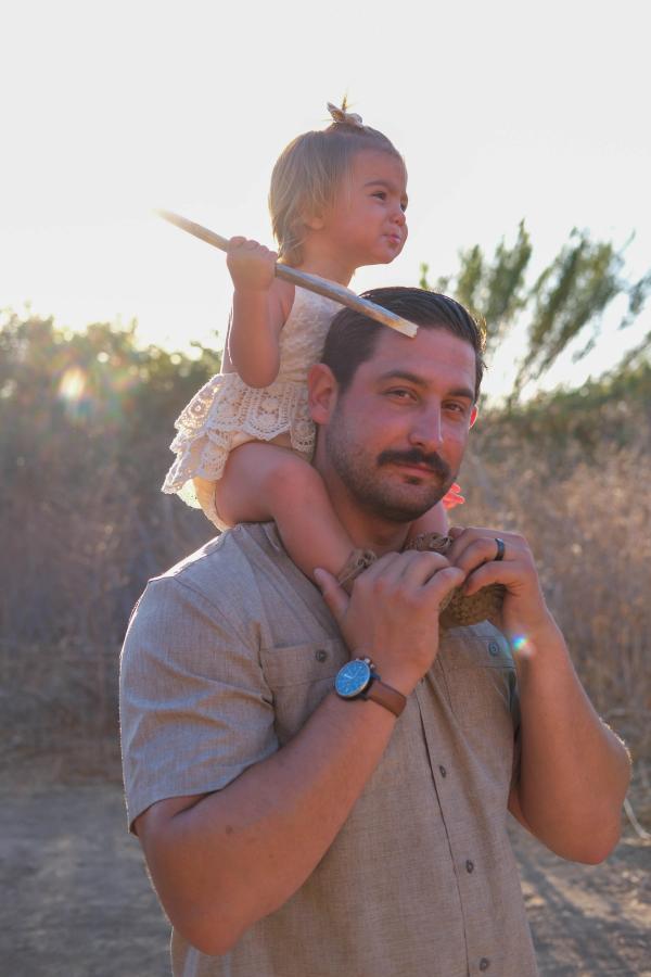 Little girl riding on her dad’s shoulders at sunset