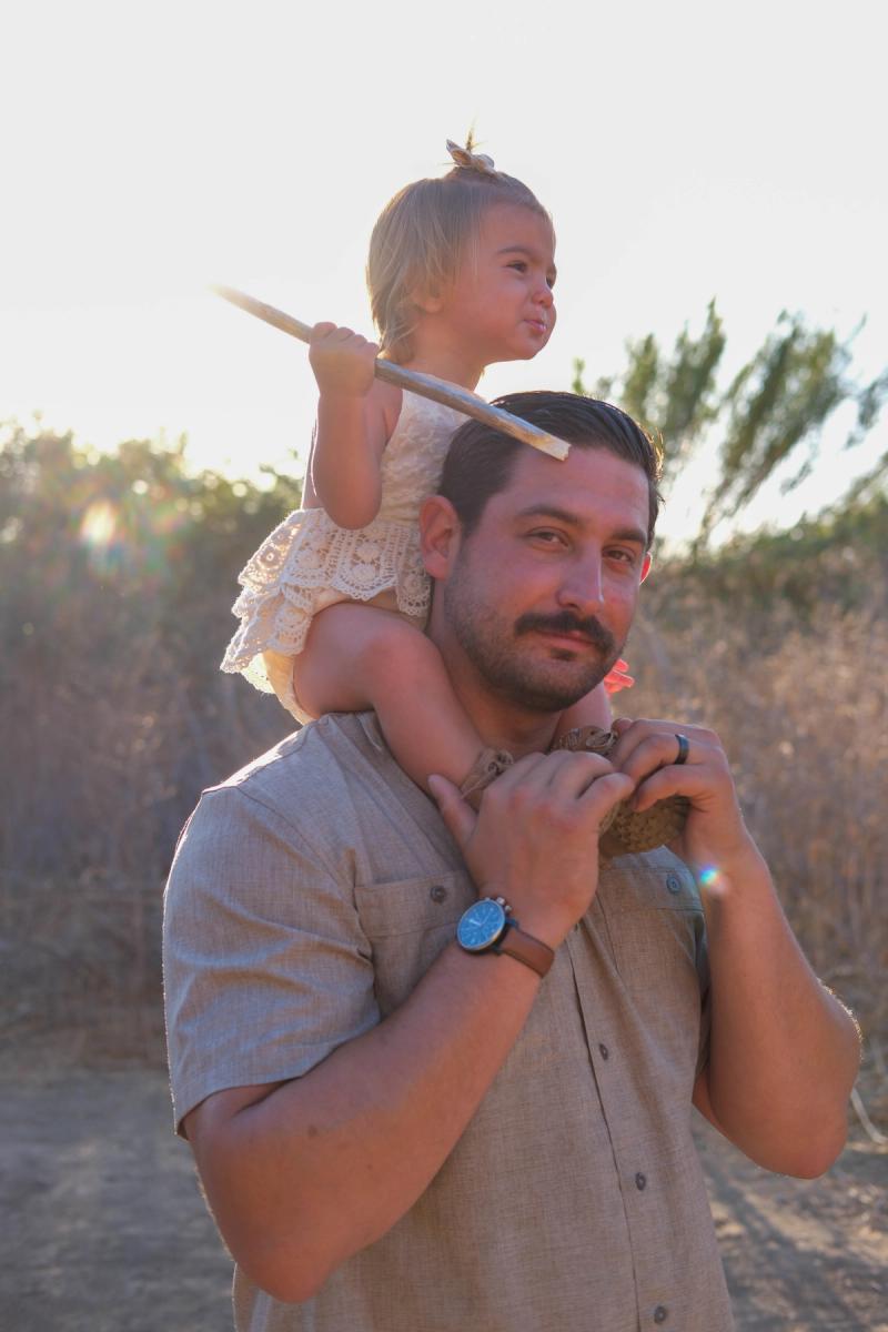 Little girl riding on her dad’s shoulders at sunset