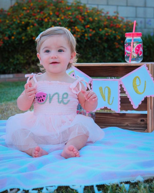 Birthday girl sitting on a blanket in front of a crate with a "one" banner
