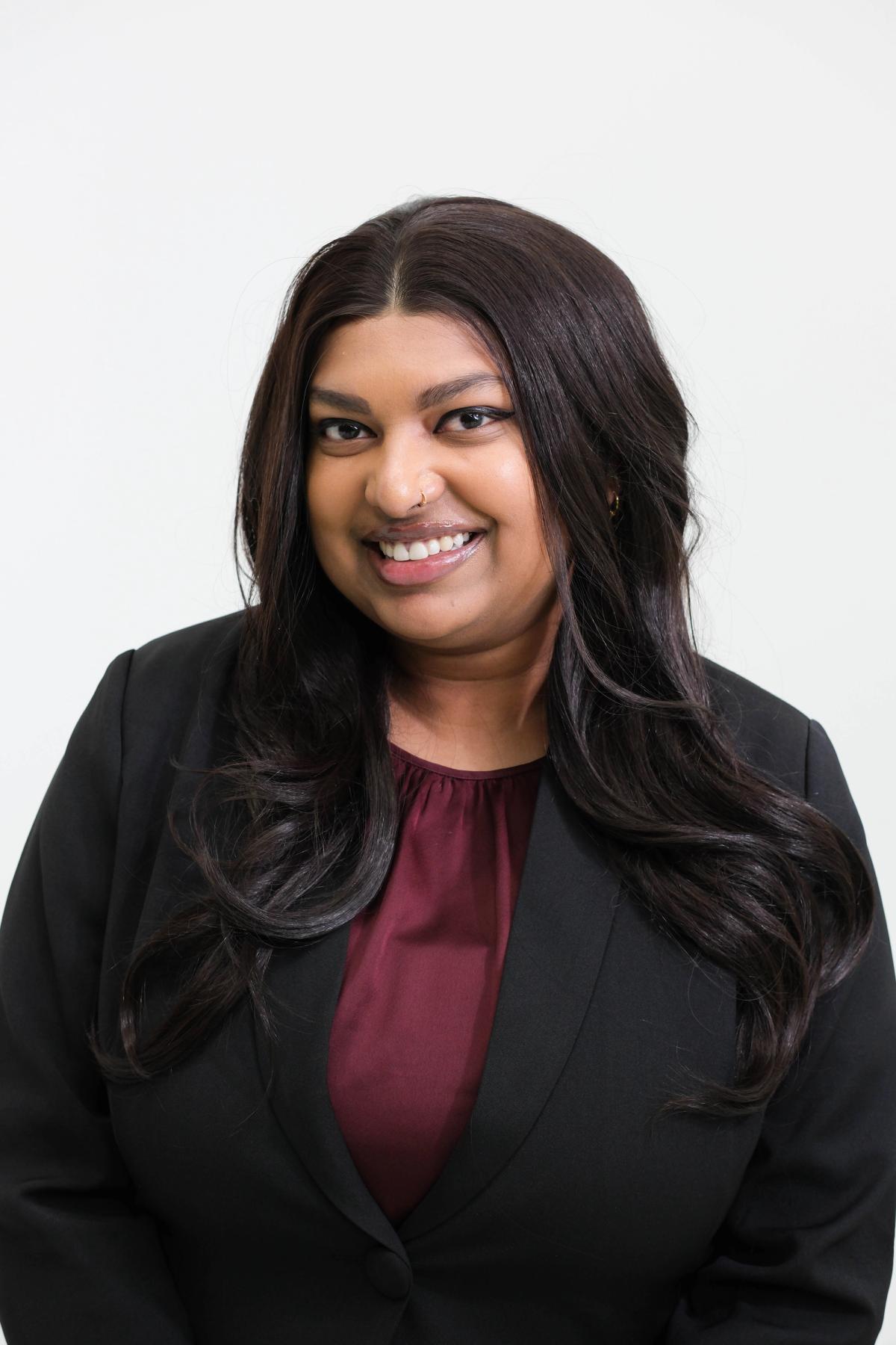 Smiling studio headshot of a woman in a black blazer and burgundy blouse
