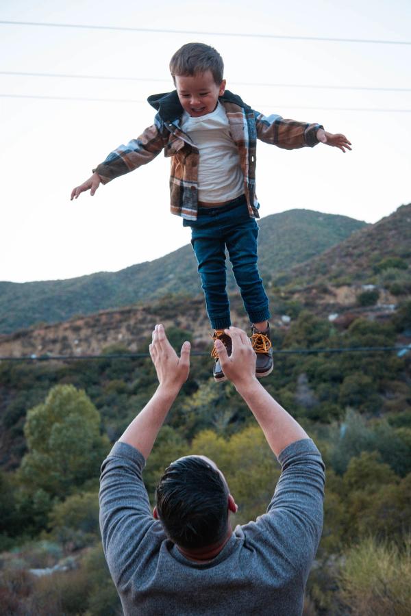 Dad tossing his son into the air in a sunlit field