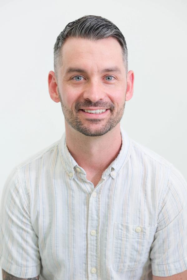 Smiling studio headshot of a man in a light striped button-down