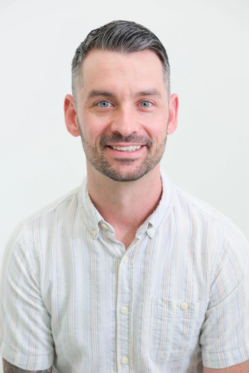 Smiling studio headshot of a man in a light striped button-down