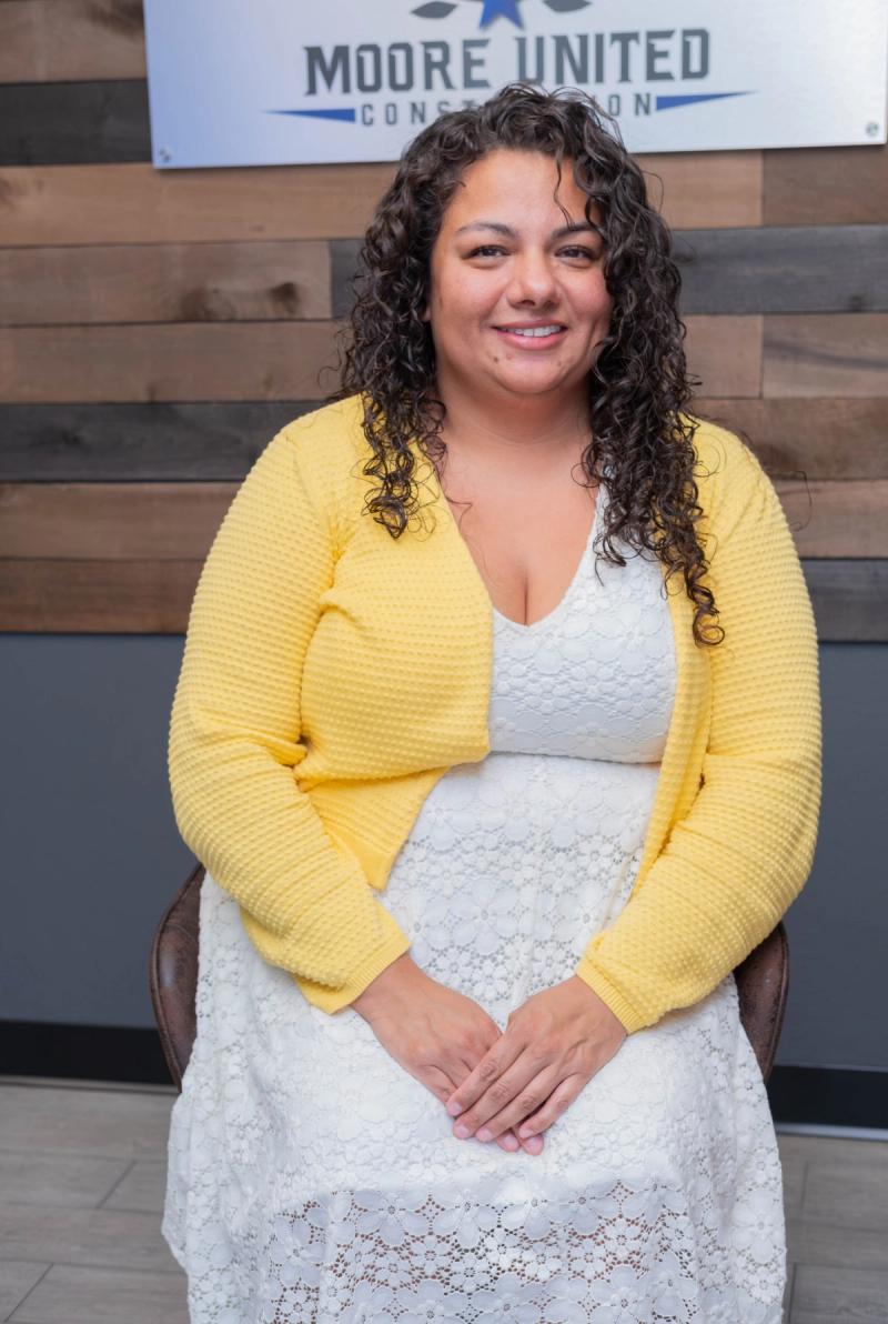 Team member in a yellow cardigan seated in front of a reclaimed wood wall