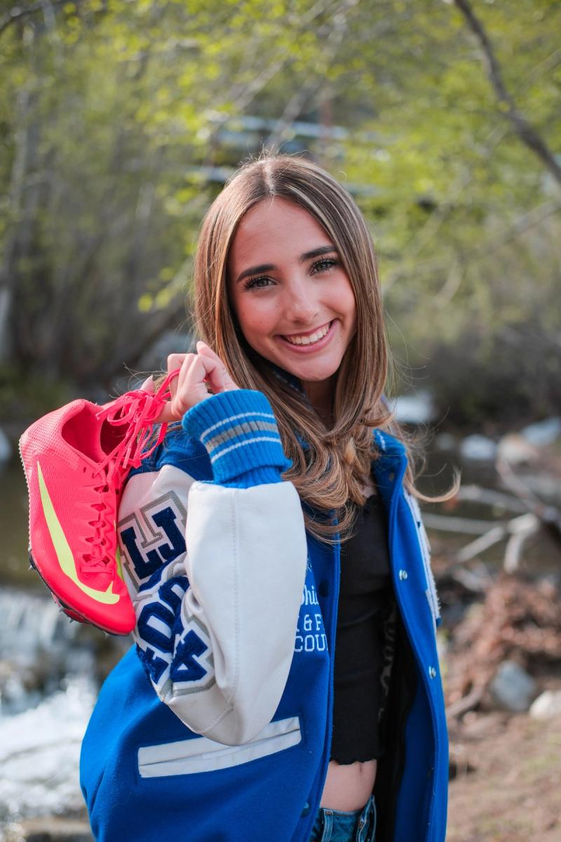 Senior holding up her red track spikes in her letterman jacket