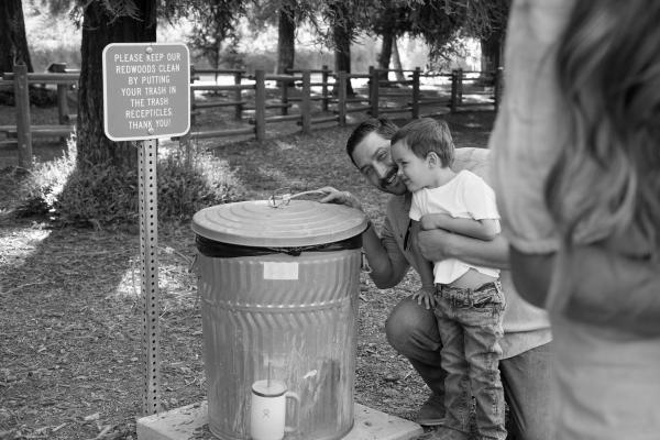 Black and white photo of a dad helping his son at a campground water spigot
