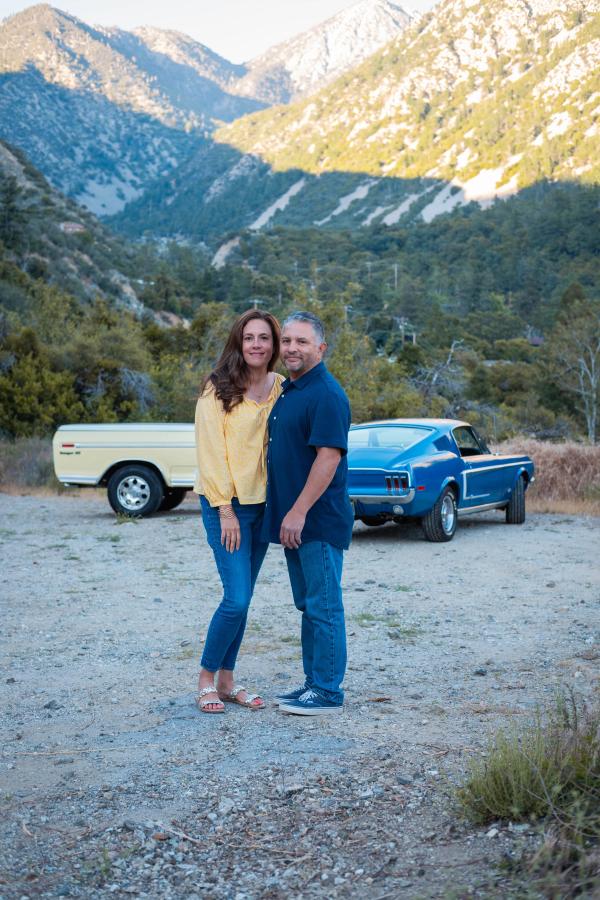 Couple smiling in front of both cars with the mountains behind