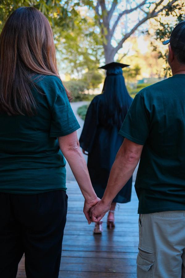 Graduate walking hand in hand with her parents, seen from behind