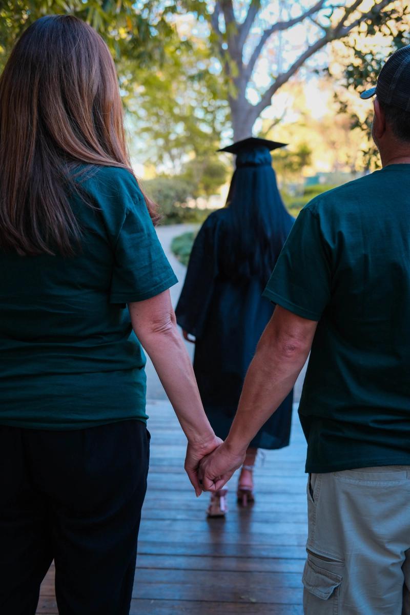 Graduate walking hand in hand with her parents, seen from behind