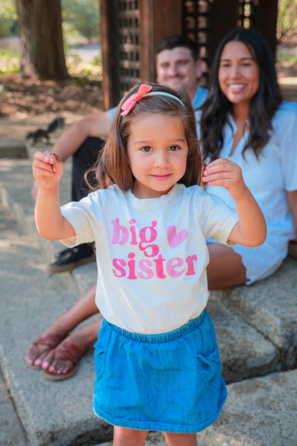 Little girl in a “big sister” shirt with her parents behind her