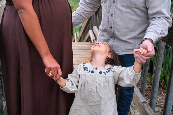 Toddler looking up and giggling as her parents hold her hands