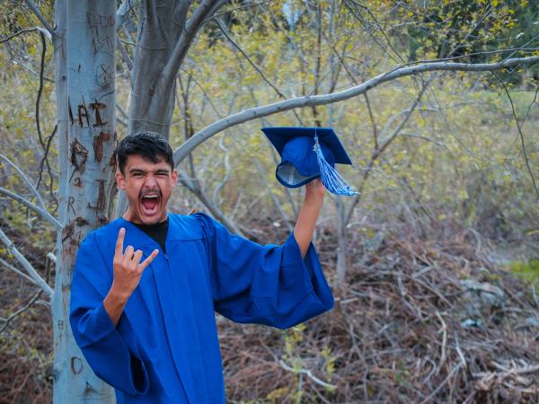 Graduate in a blue gown cheering with his cap raised high