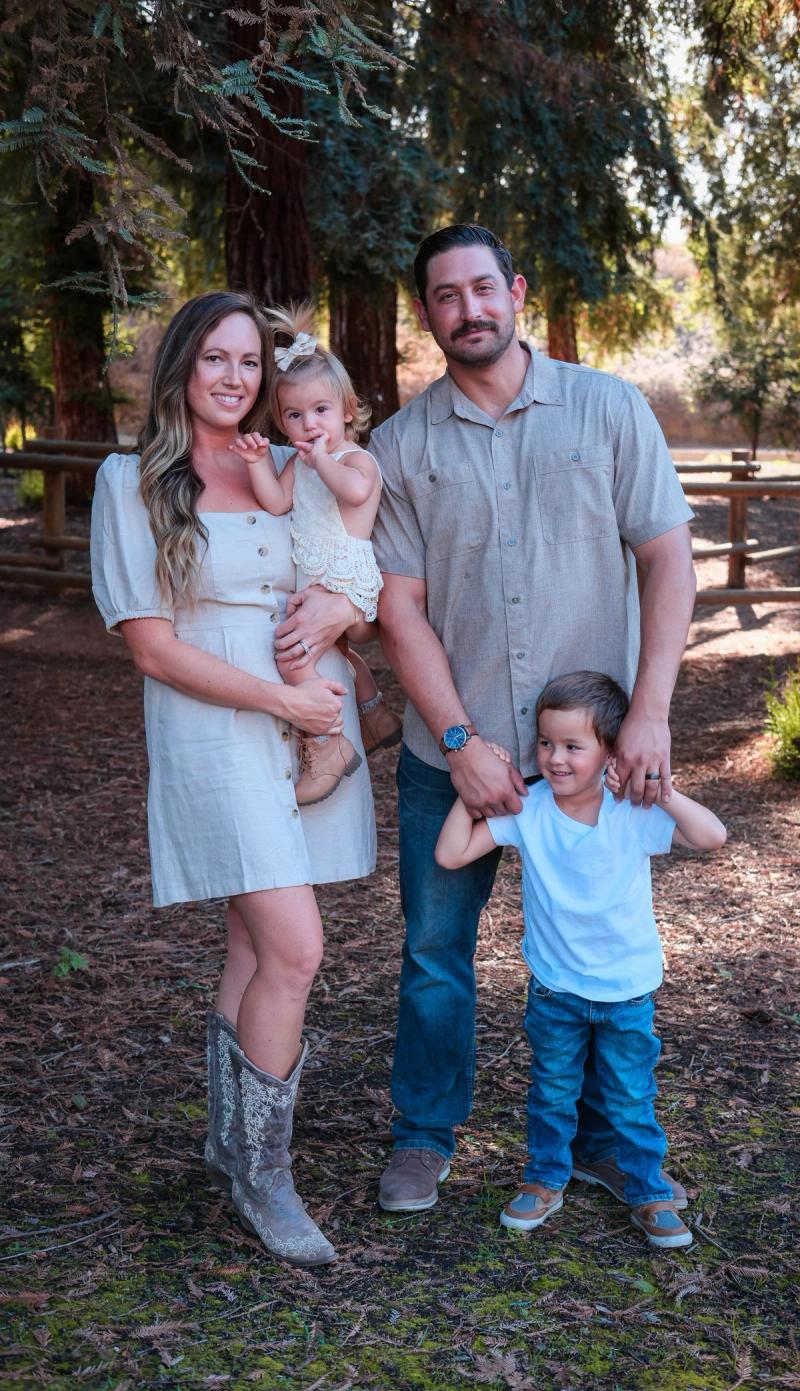 Family of four smiling together beneath tall pines