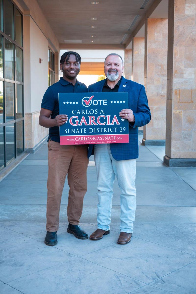 Candidate and a young volunteer holding a Vote Carlos A. Garcia sign together