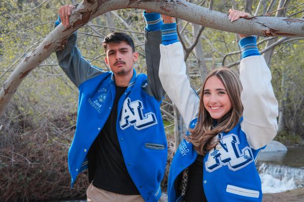 Two seniors in letterman jackets hanging from a low branch