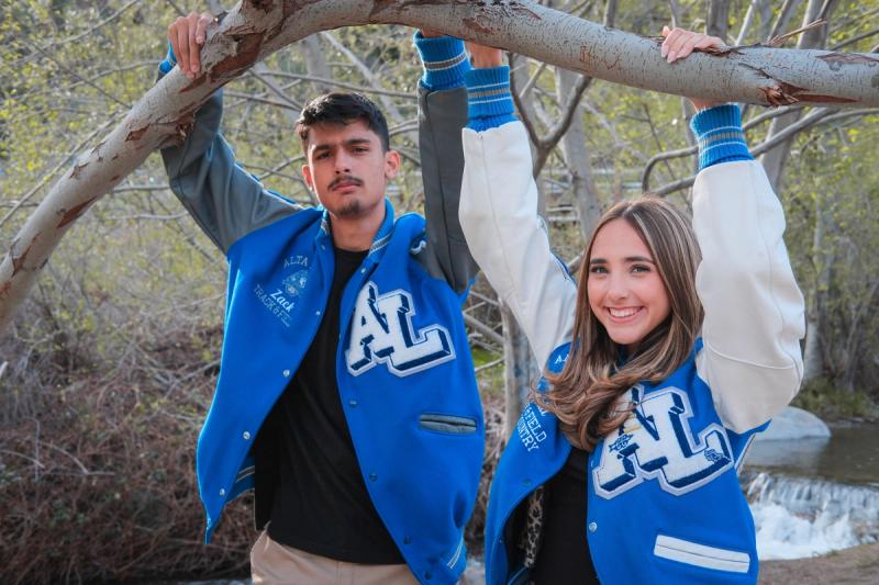 Two seniors in letterman jackets hanging from a low branch