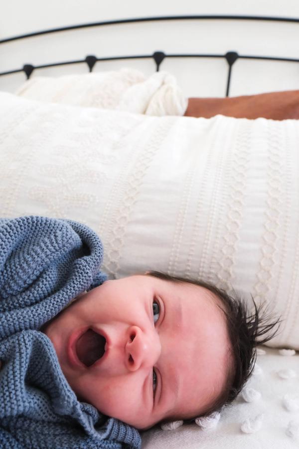Newborn yawning in a blue knit sweater on a white bed