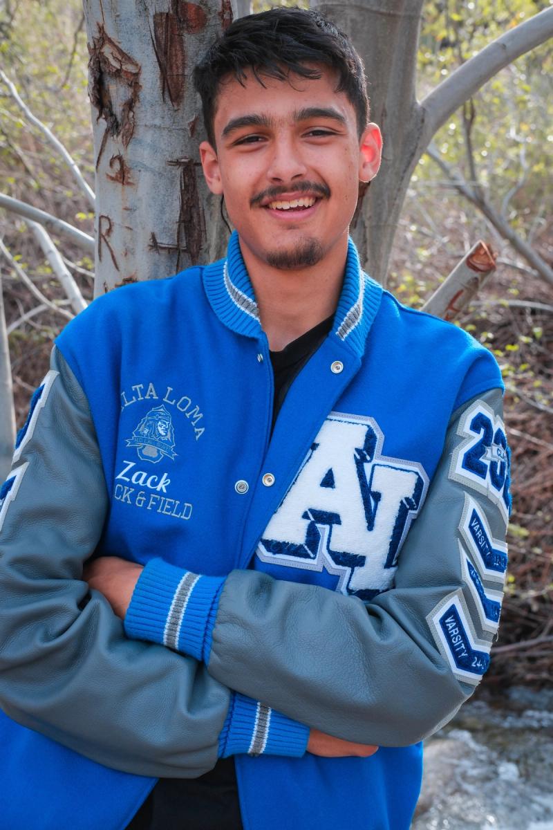 Smiling senior in his blue letterman jacket with arms crossed