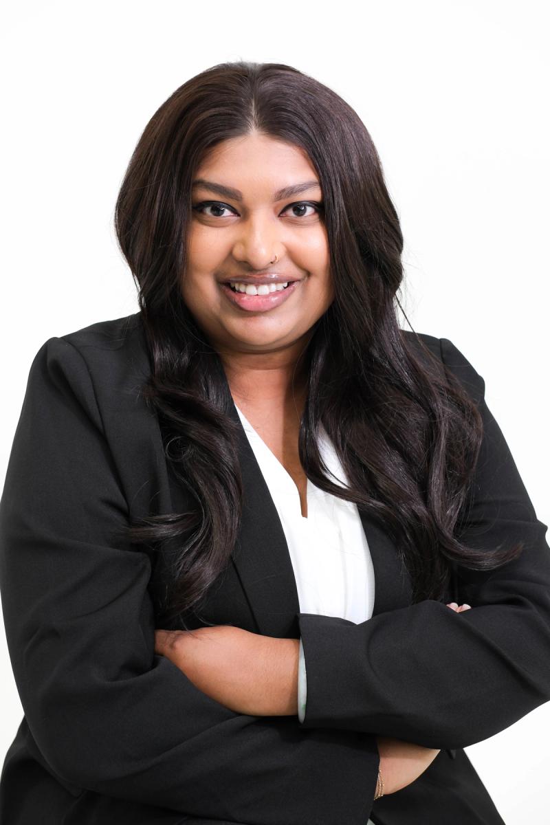 Woman in a black blazer and white blouse with arms crossed, smiling