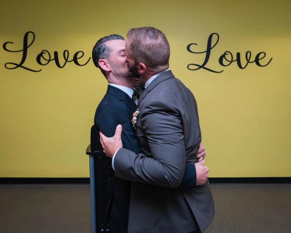 Newlyweds kissing in front of the Love Is Love wall